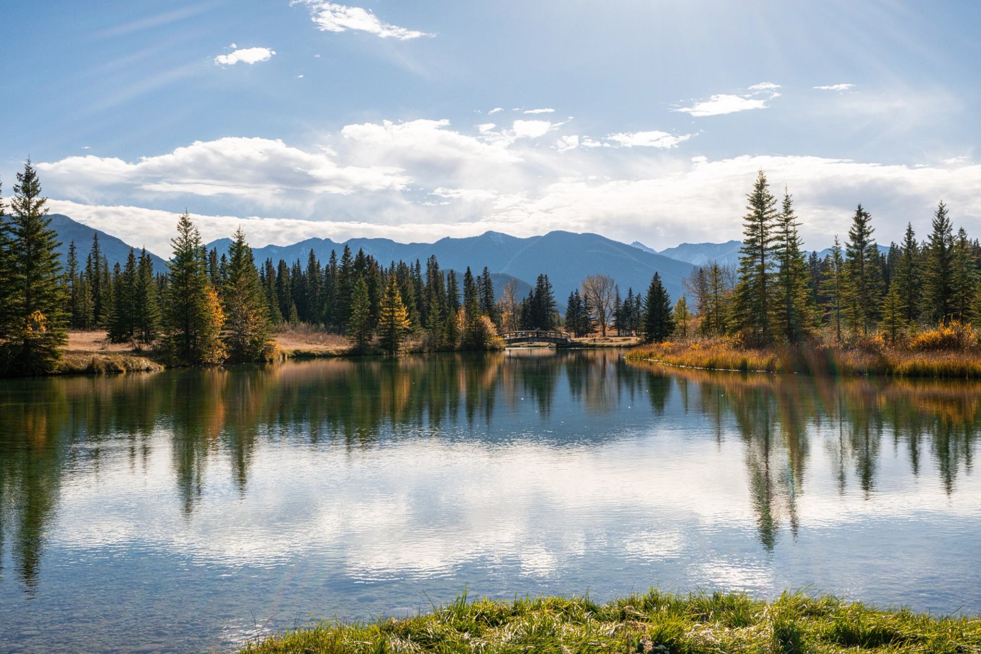 Green and gold trees reflect off the water at Cascade Ponds in Banff with mountains in the distance.