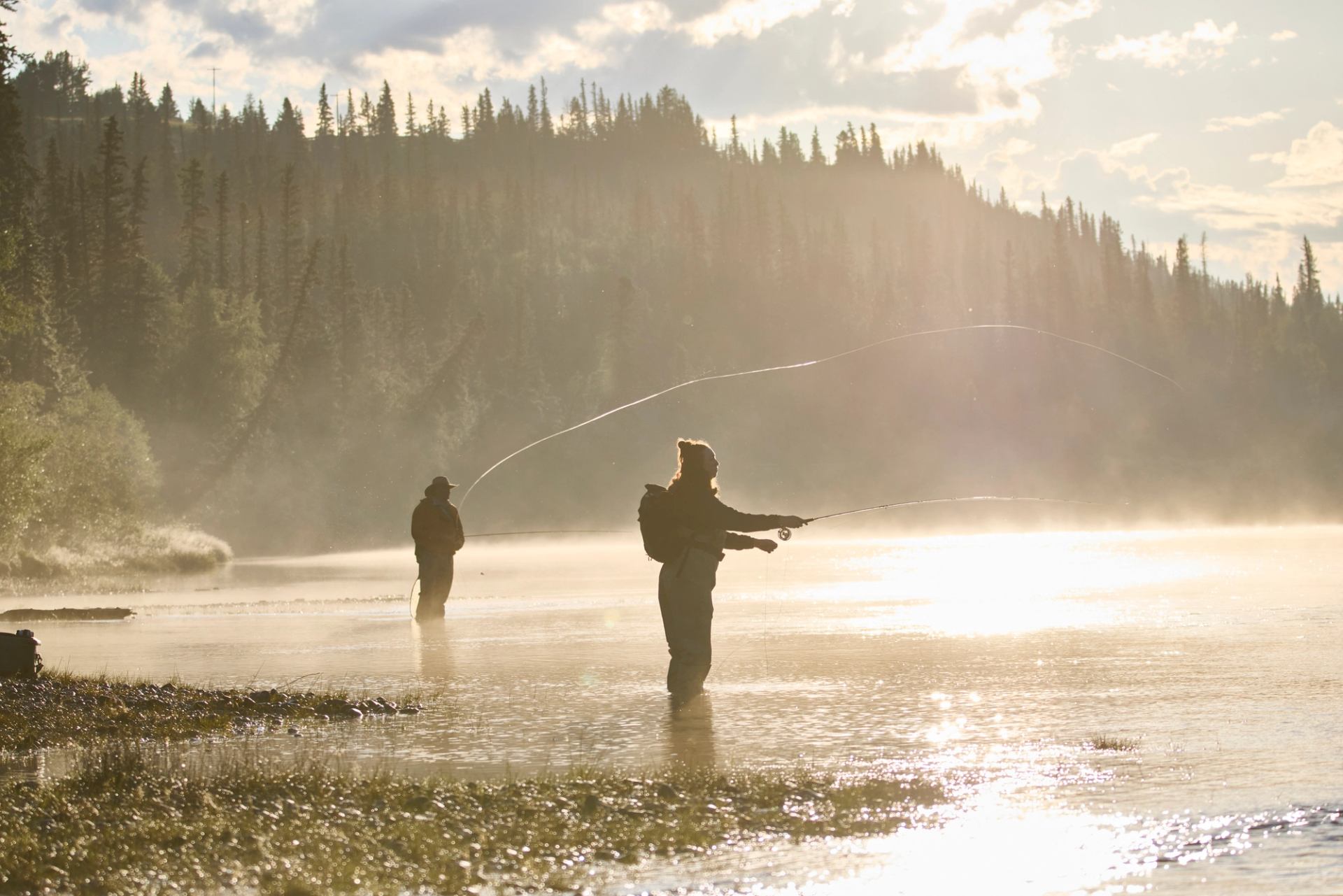 Two people fly fishing in the river with the sun reflecting off the water