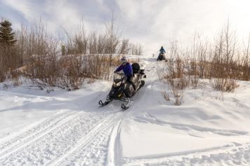Two people ride snowmobiles over a snowy trail in Whitecourt.
