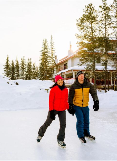 A family of four, parents holding hands and smiling, ice skating on an outdoor rink.