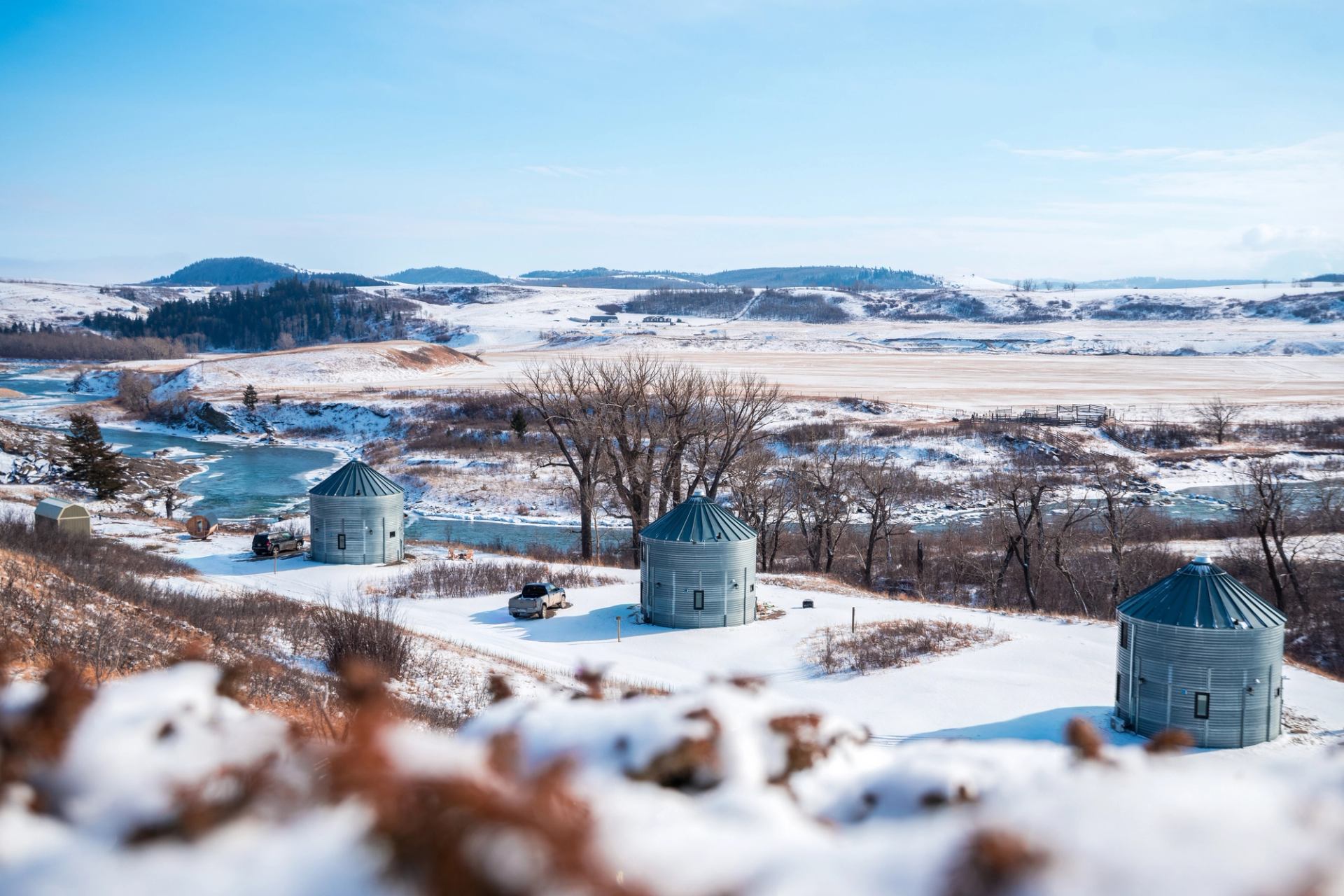 Winter landscape with silos, river, and snow-covered hills.