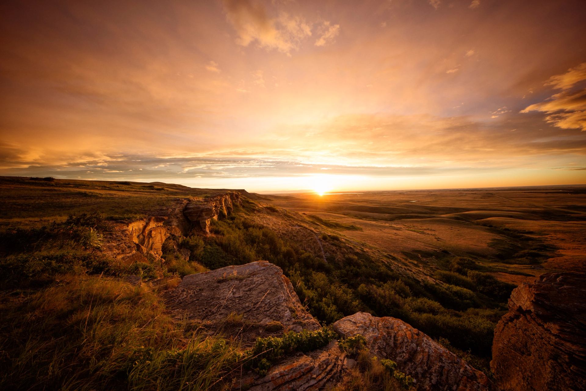 The sun sets over rock cliffs covered in grass and bushes.