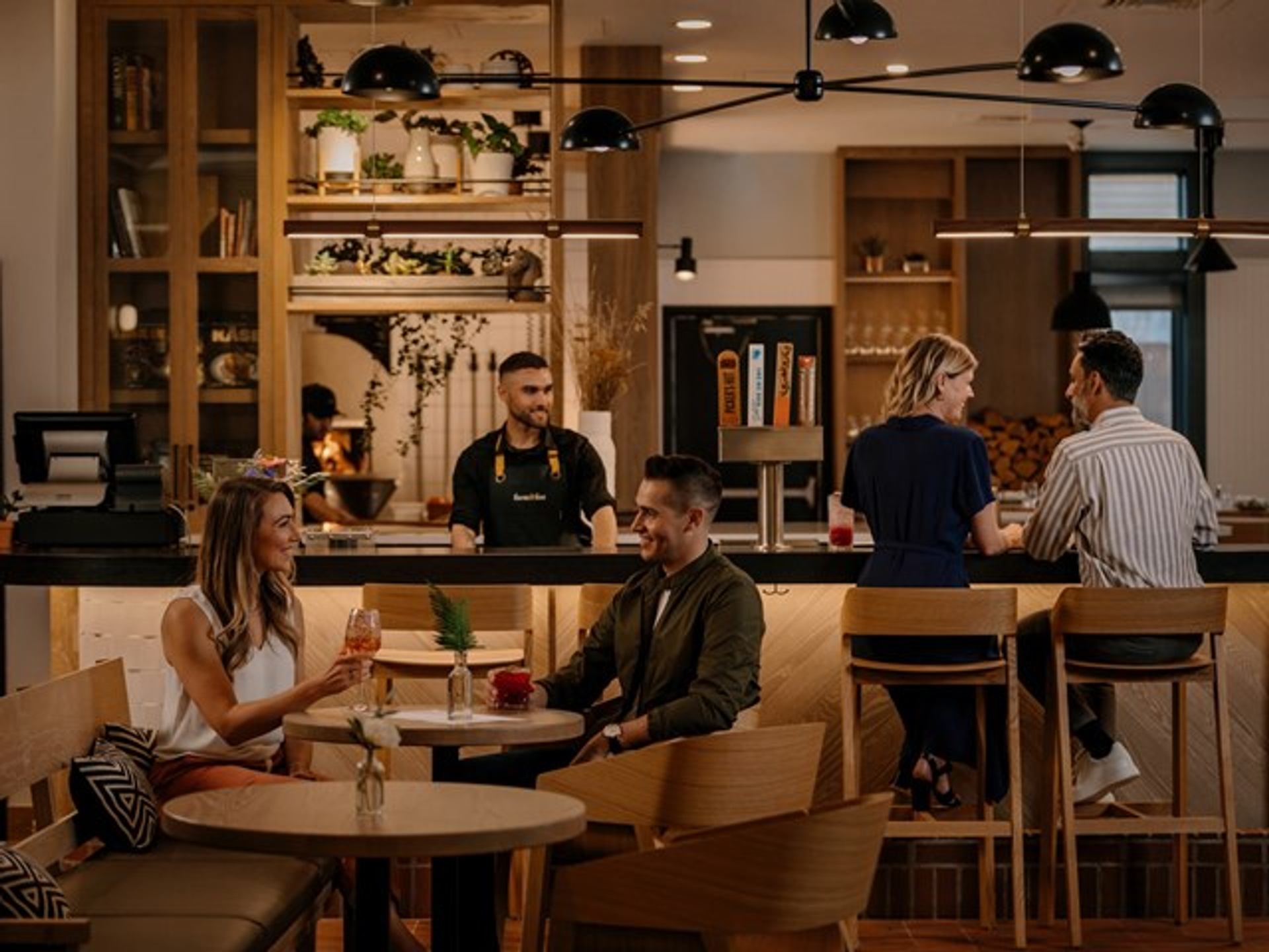 A couple sits at a table at Farm & Fire restaurant with other guests and bartender in the background.