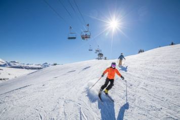 Couple skiing down hill with sun above