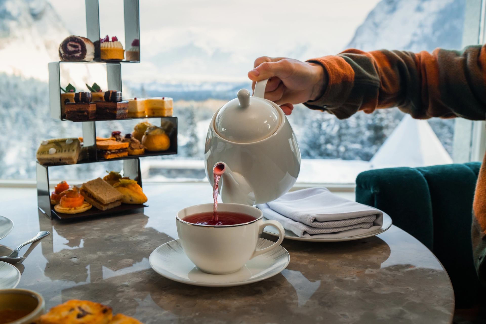 Tea being poured with desserts on a table, featuring a mountain landscape outside the window at Fairmont Banff Springs.