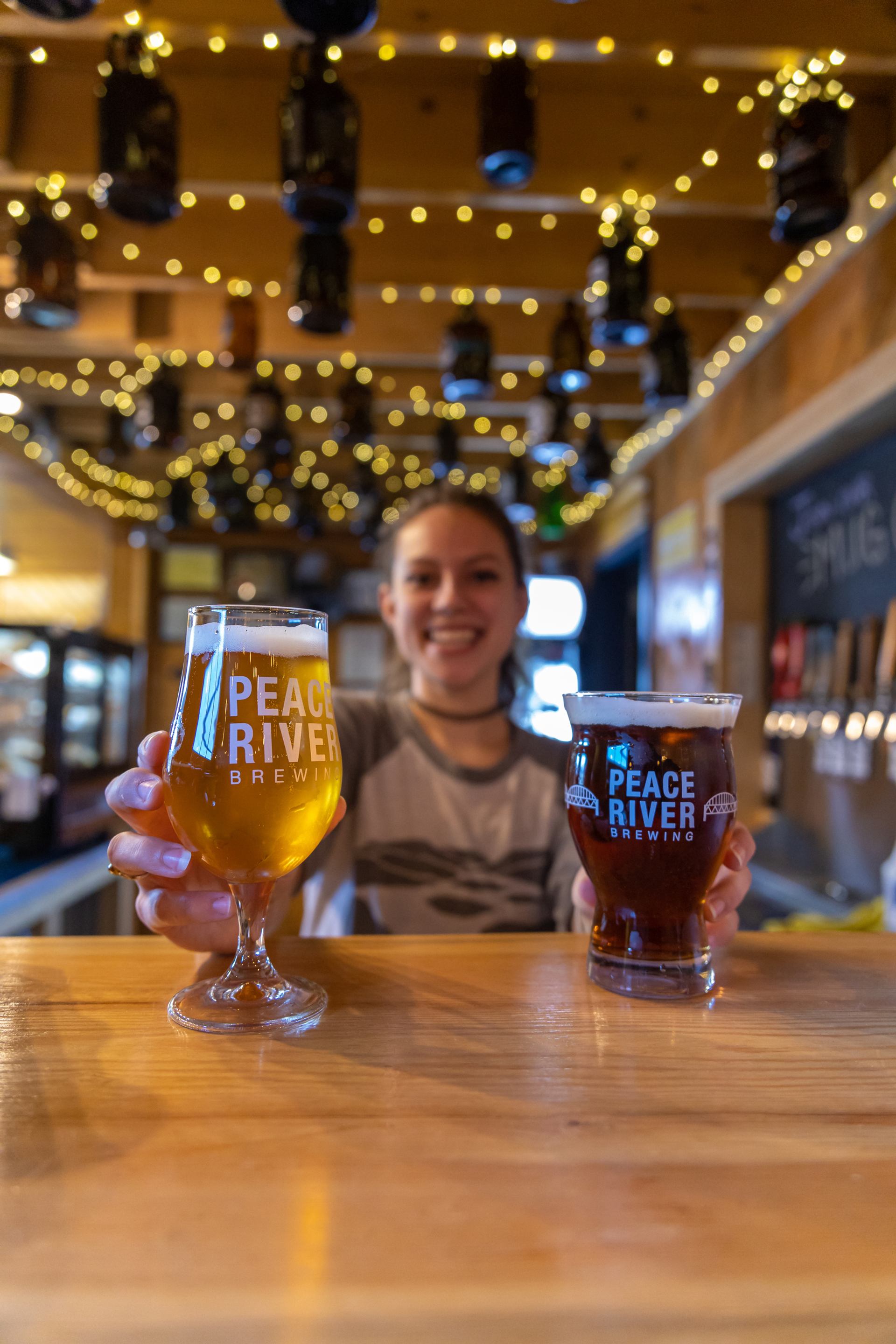 Woman holding two beverages inside of the Peace River Brewing brewery.