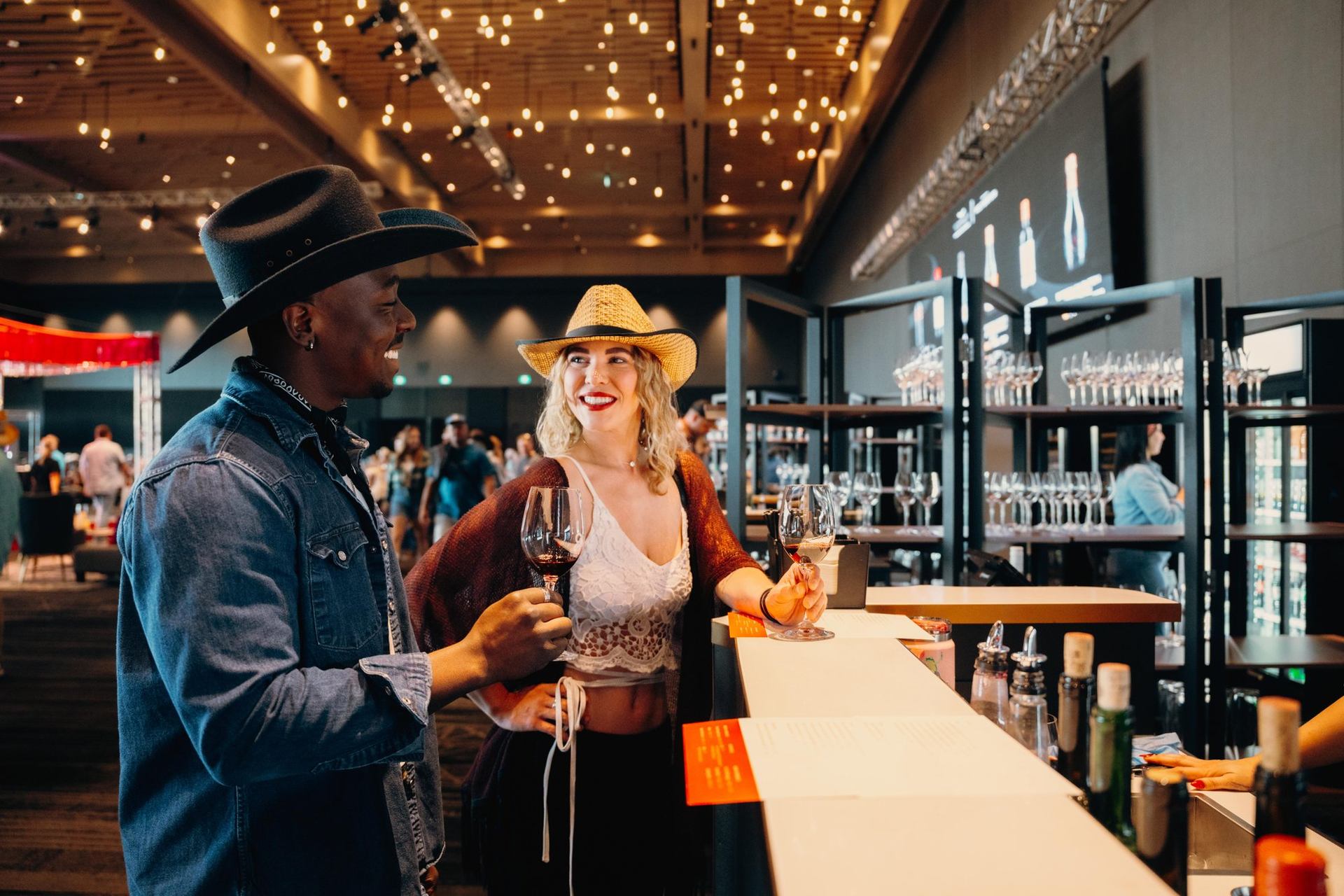Two guests in cowboy hats hold wine glasses in ballroom at Calgary's BMO Centre.