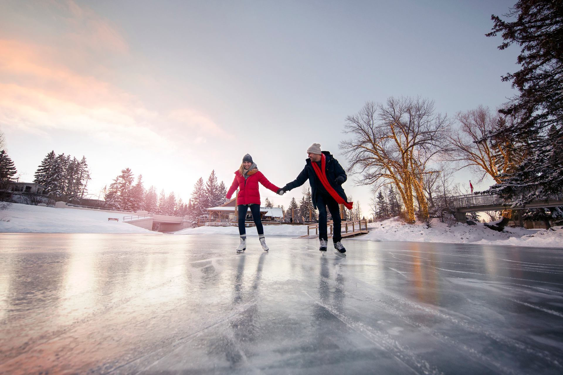 Two people skating on a rink at sunset with the trees in the background.