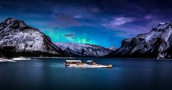 Northern lights shine over mountains and the floating dock on Lake Minnewanka at night in Banff National Park.