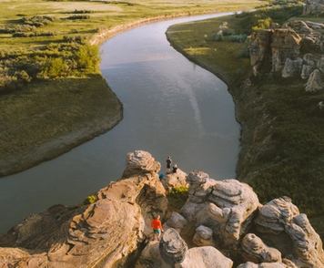 Distance shot of people hiking and standing on hoodoos overlooking a river view