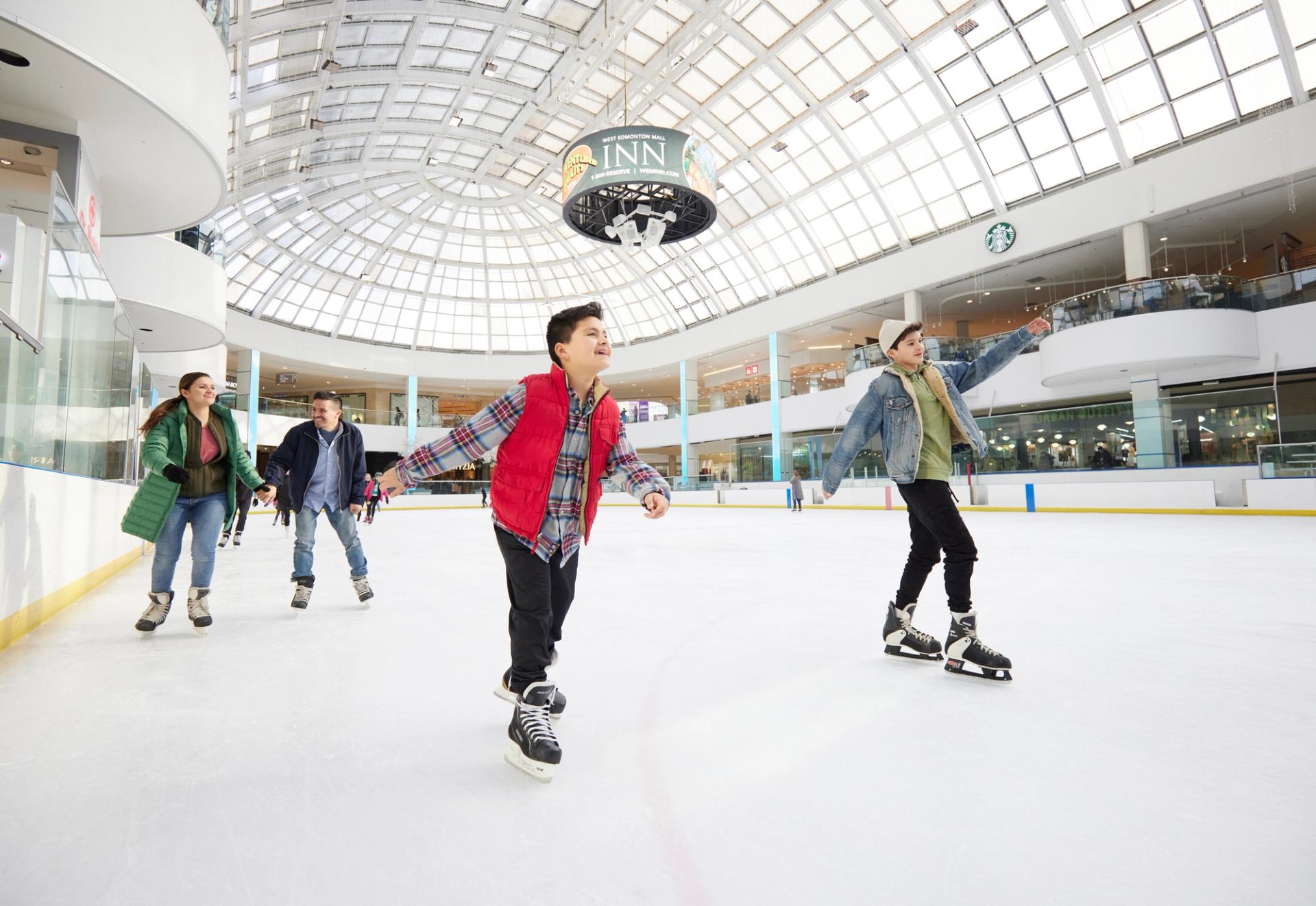 Two kids and their parents skate indoors under a huge glass skylight at the Ice Palace in Edmonton.