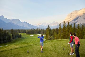 Three men golf on a course in the mountains.