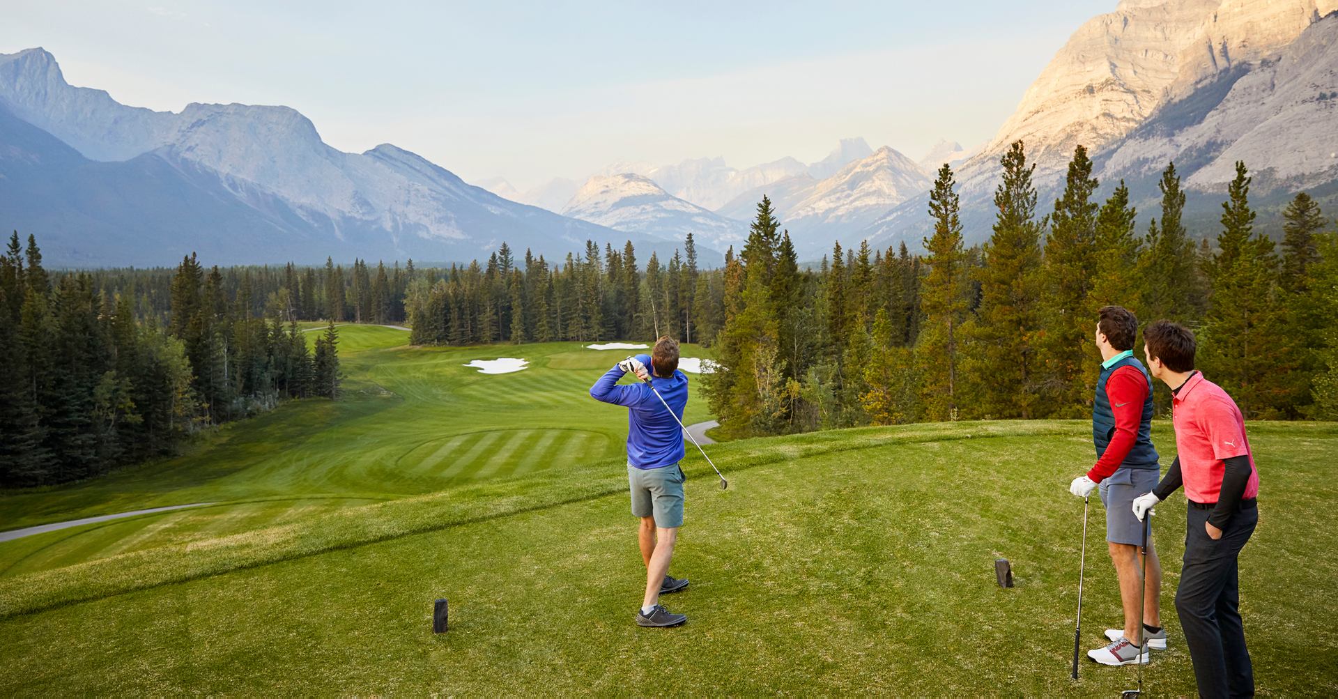 Three men golf on a course in the mountains.