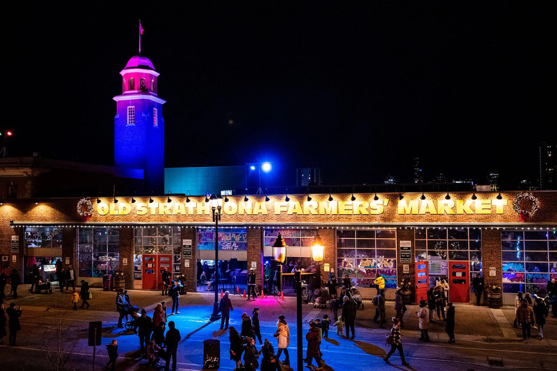 A crowd of people walks by a farmers’ market at night