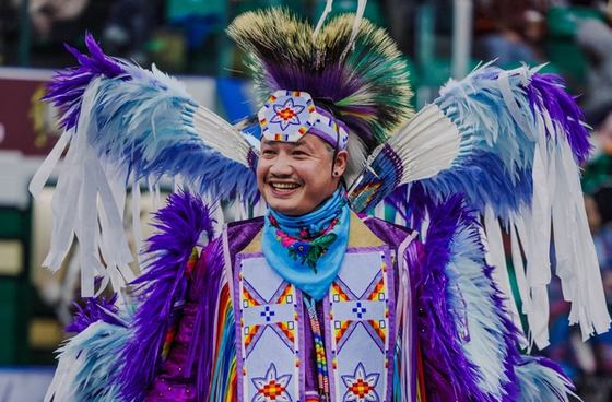 A young powwow dancer in colourful regalia, featuring lime green, bright yellow and other colours, performs at a powwow.