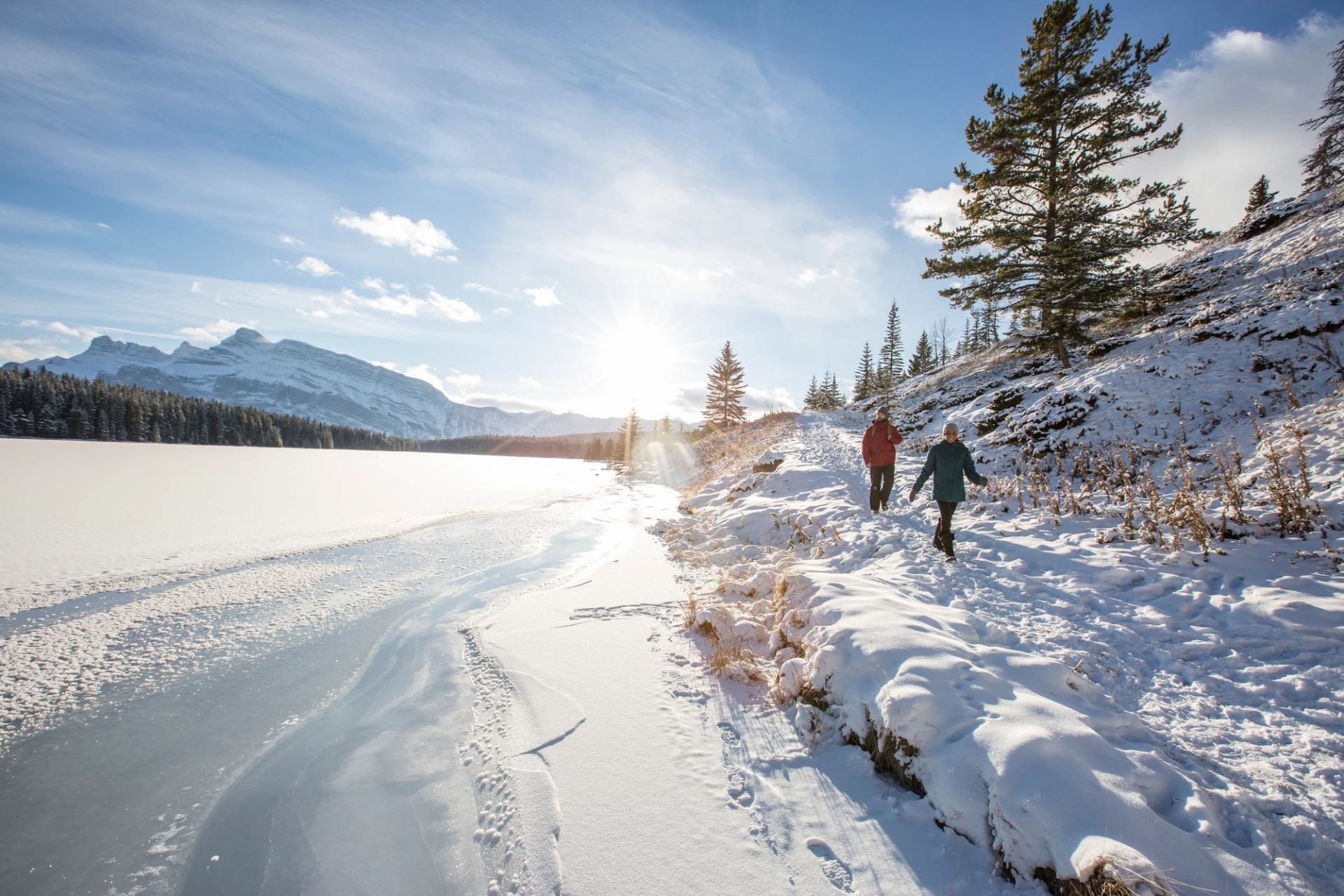 A couple winter hiking along a frozen Two Jack Lake on a sunny winter day.