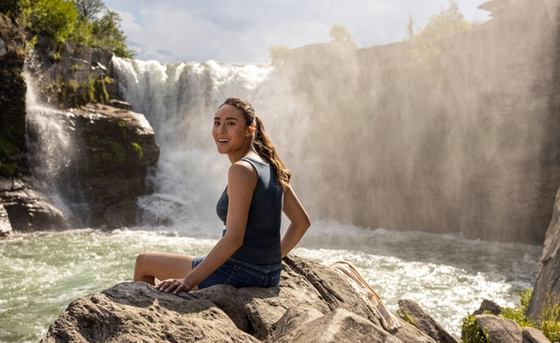 A woman smiles while sitting on a rock near Lundbreck Falls.