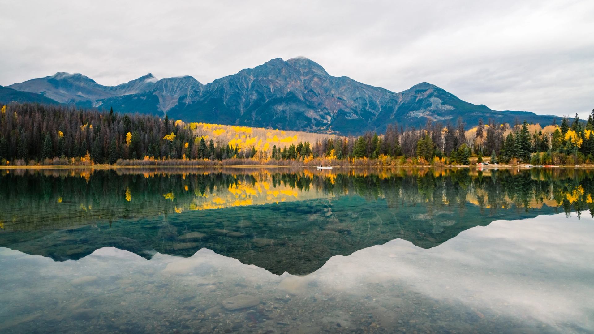 Two people in a white canoe paddle on Patricia Lake in Jasper National Park, with mountains in the background.