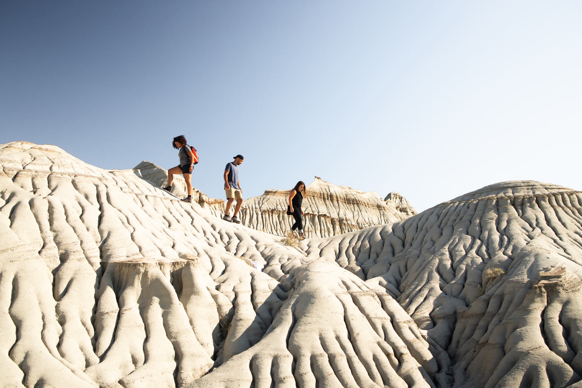 A group of four visitors walk over ancient hoodoos while exploring Dinosaur Provincial Park within the Canadian Badlands.
