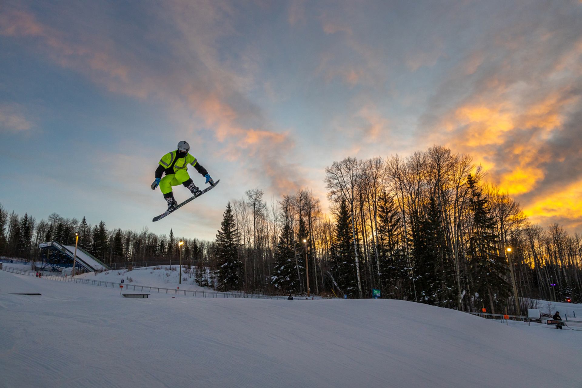 A snowboarder catches some air at ski resort as the sun sets.