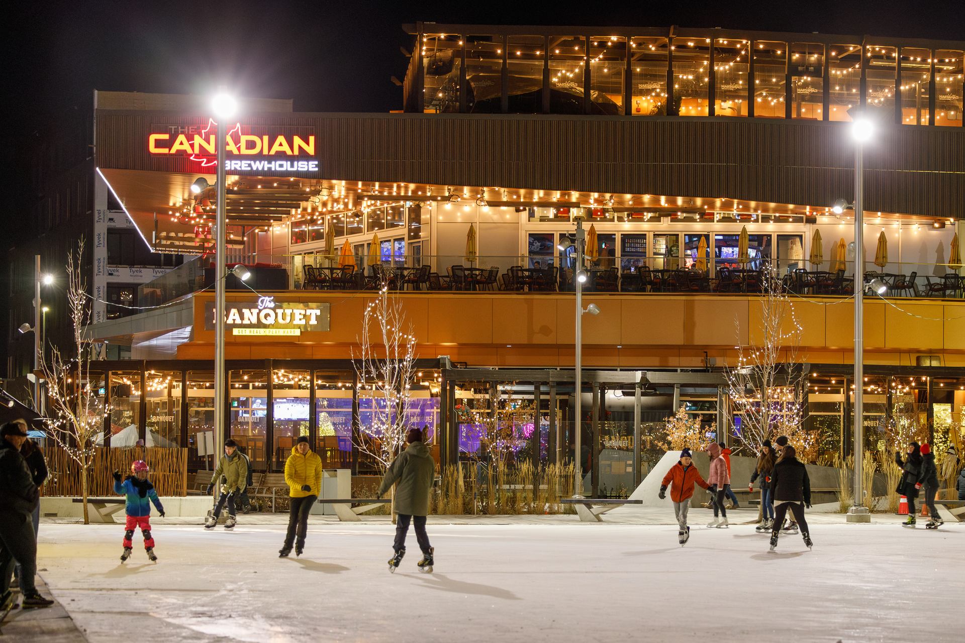 People skate the University District ice rink during the evening with restaurants in the background.
