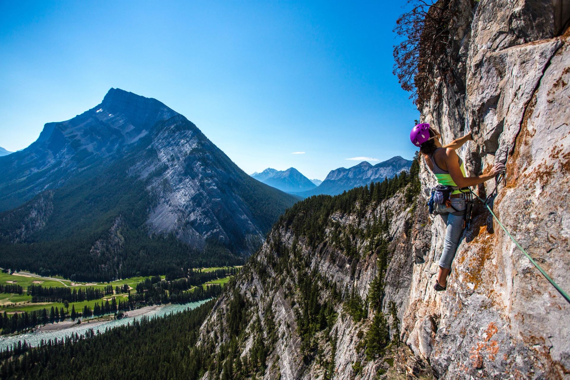 Women rock climbing up the side of a mountain with a river and mountain view in the background