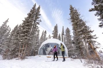 Couple crosscountry skiing outside a glamping dome at Elevated Escapes.