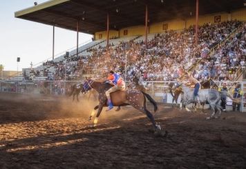 Two riders thunder on horseback toward the exchange zone, where teammates stand ready during a relay race.
