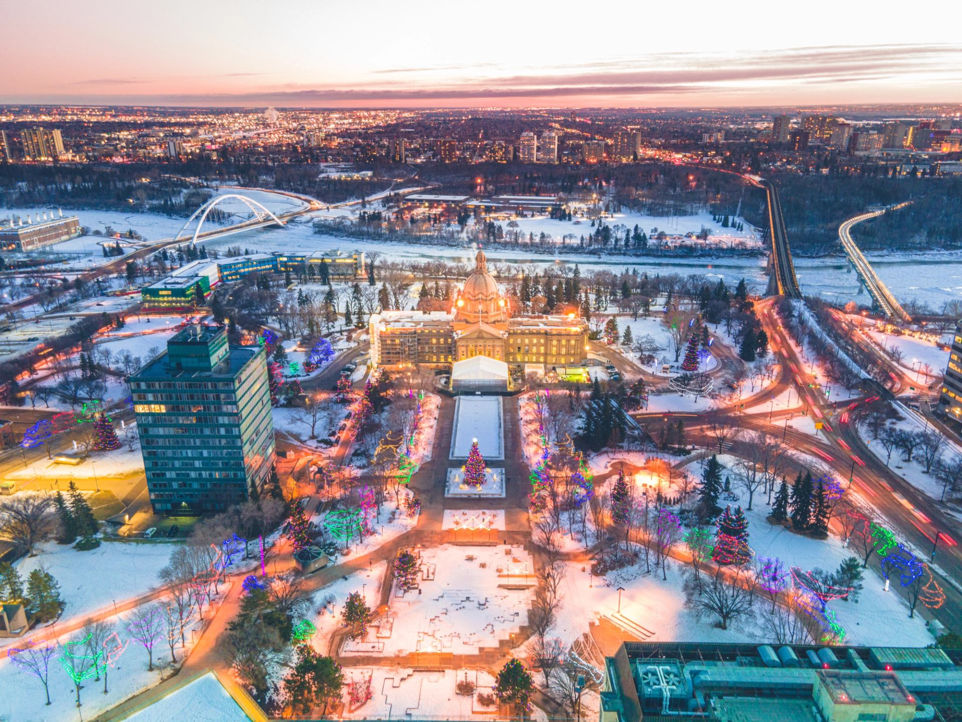 A view from above of the snow-covered Alberta Legislature Grounds sprinkled with holiday lights and the warm glow of sundown.