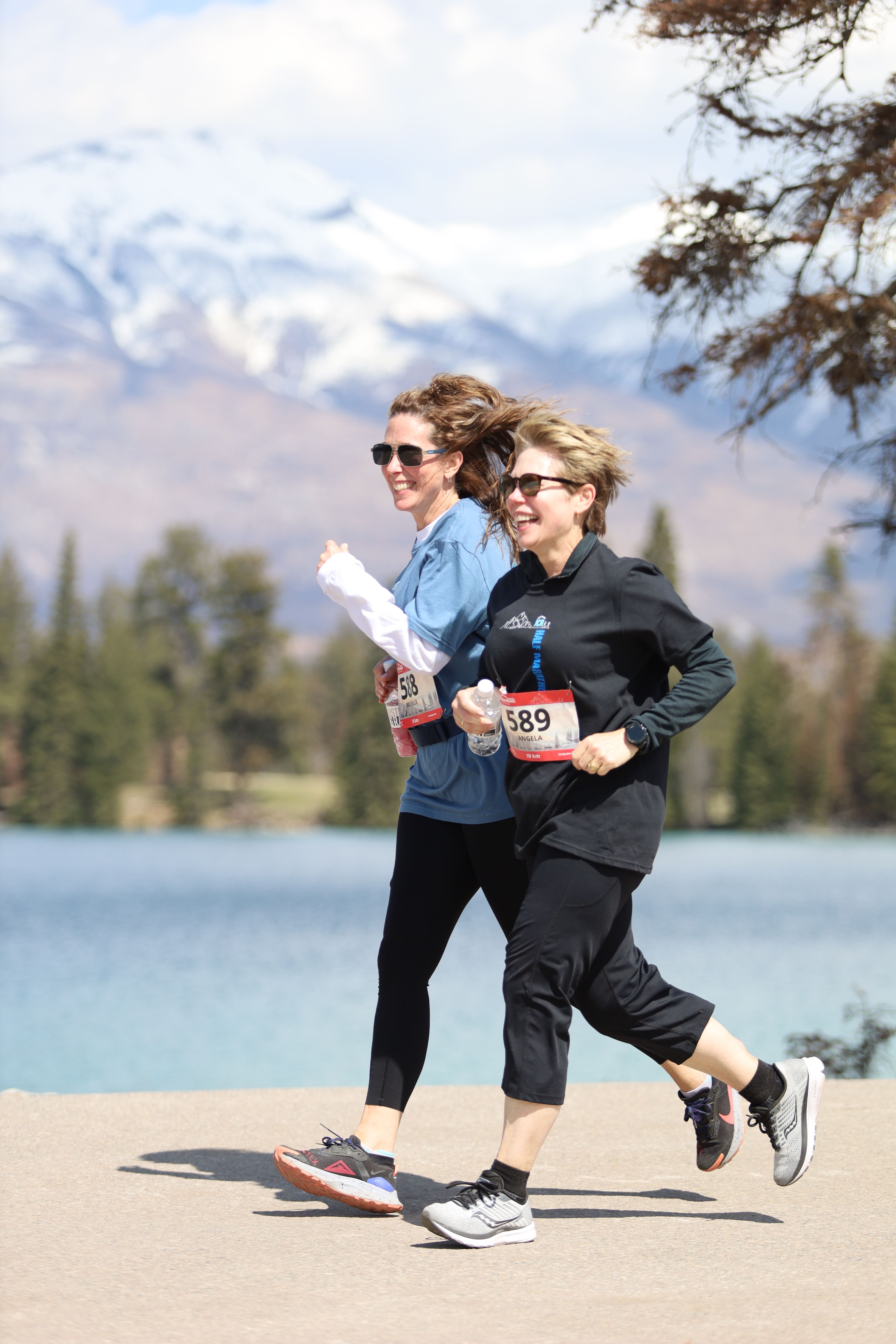 Two runners smile as they run past a lake in Jasper.