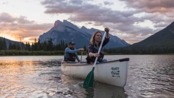 Two people paddle a canoe at Vermilion Lakes in Banff at sunset.
