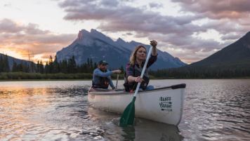 Two people paddle a canoe at Vermilion Lakes in Banff at sunset.