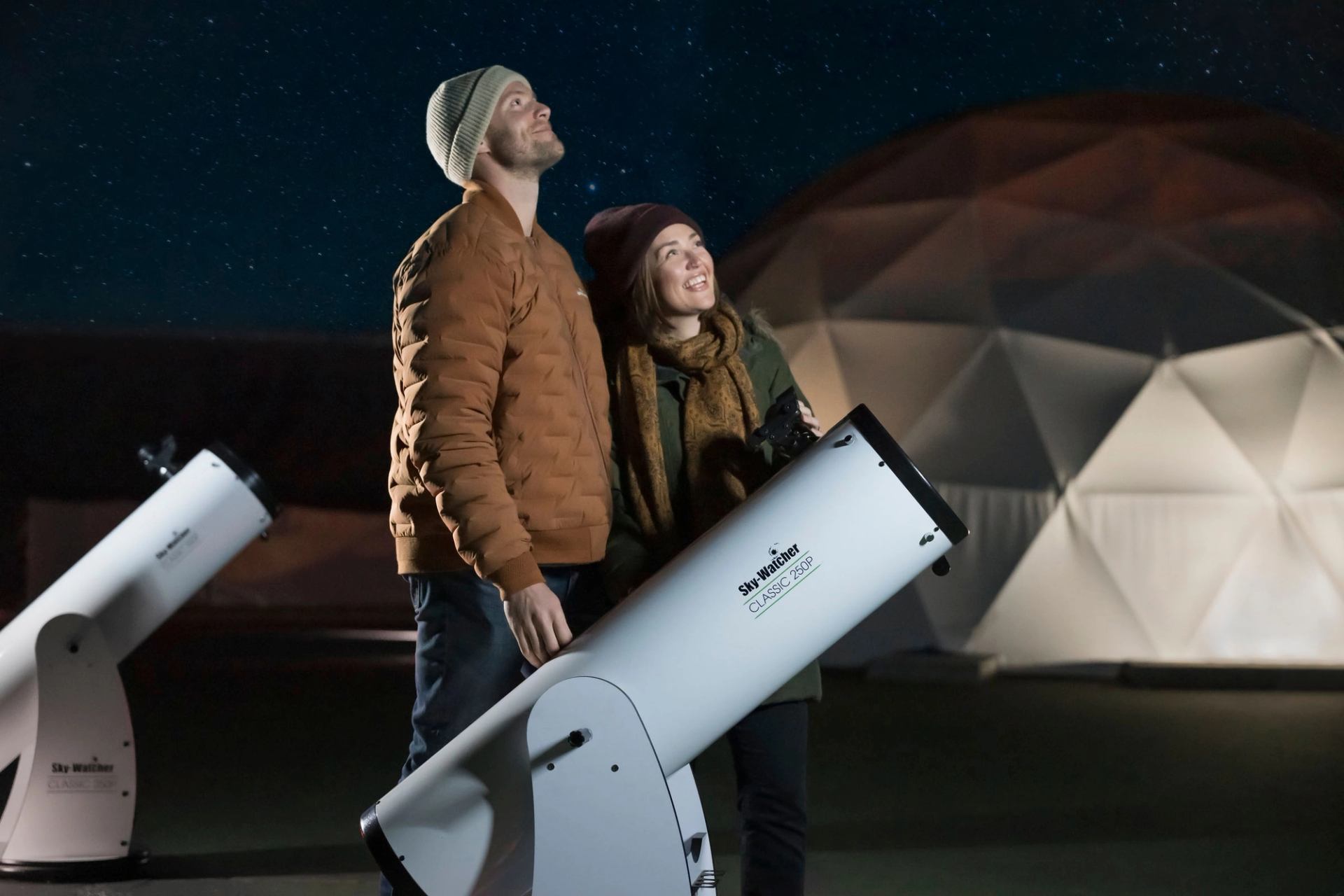 Young couple outside looking skyward, telescopes on ground, at the Jasper Planetarium.