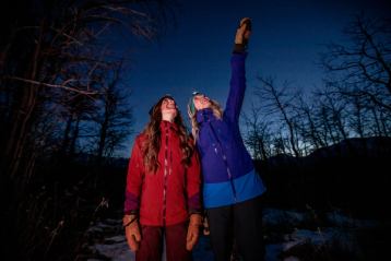 Two women looking at the night sky with one of the pointing up.