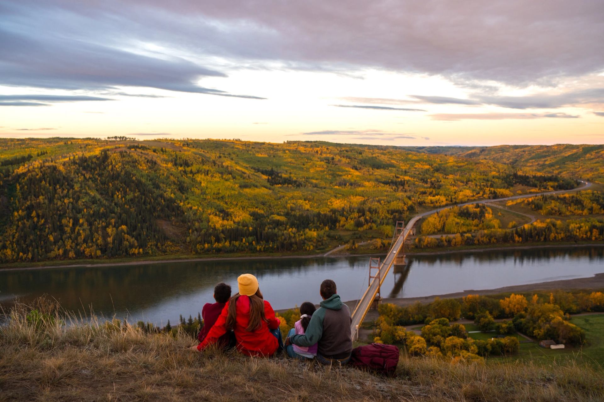 A family sitting together watching sunrise at Dunvegan Overlook with Dunvegan Bridge in the background.