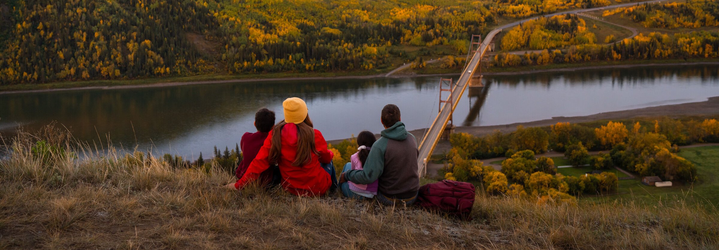 A family sitting together watching sunrise at Dunvegan Overlook with Dunvegan Bridge in the background.