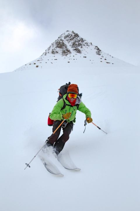 Person with backpack and gear, backcountry skiing with mountains in the background.