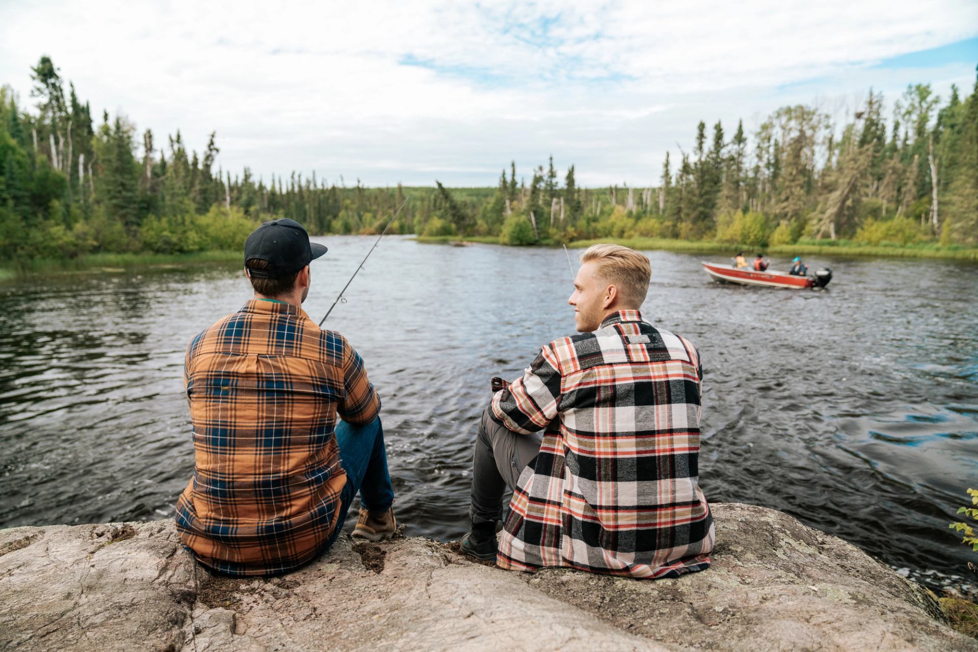 Two men sit on a dock fishing.