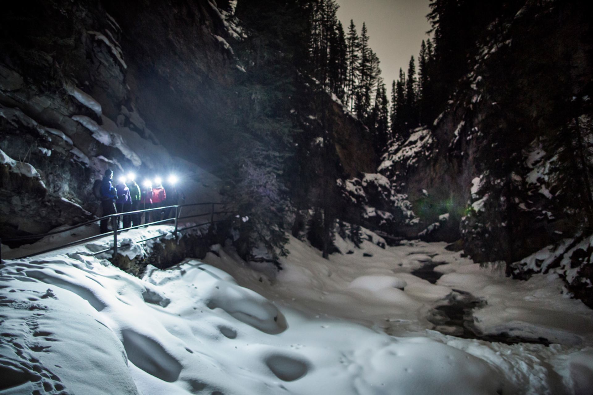 A group of people wearing headlamps takes an ice walk in Johnston Canyon at night in Banff National Park.