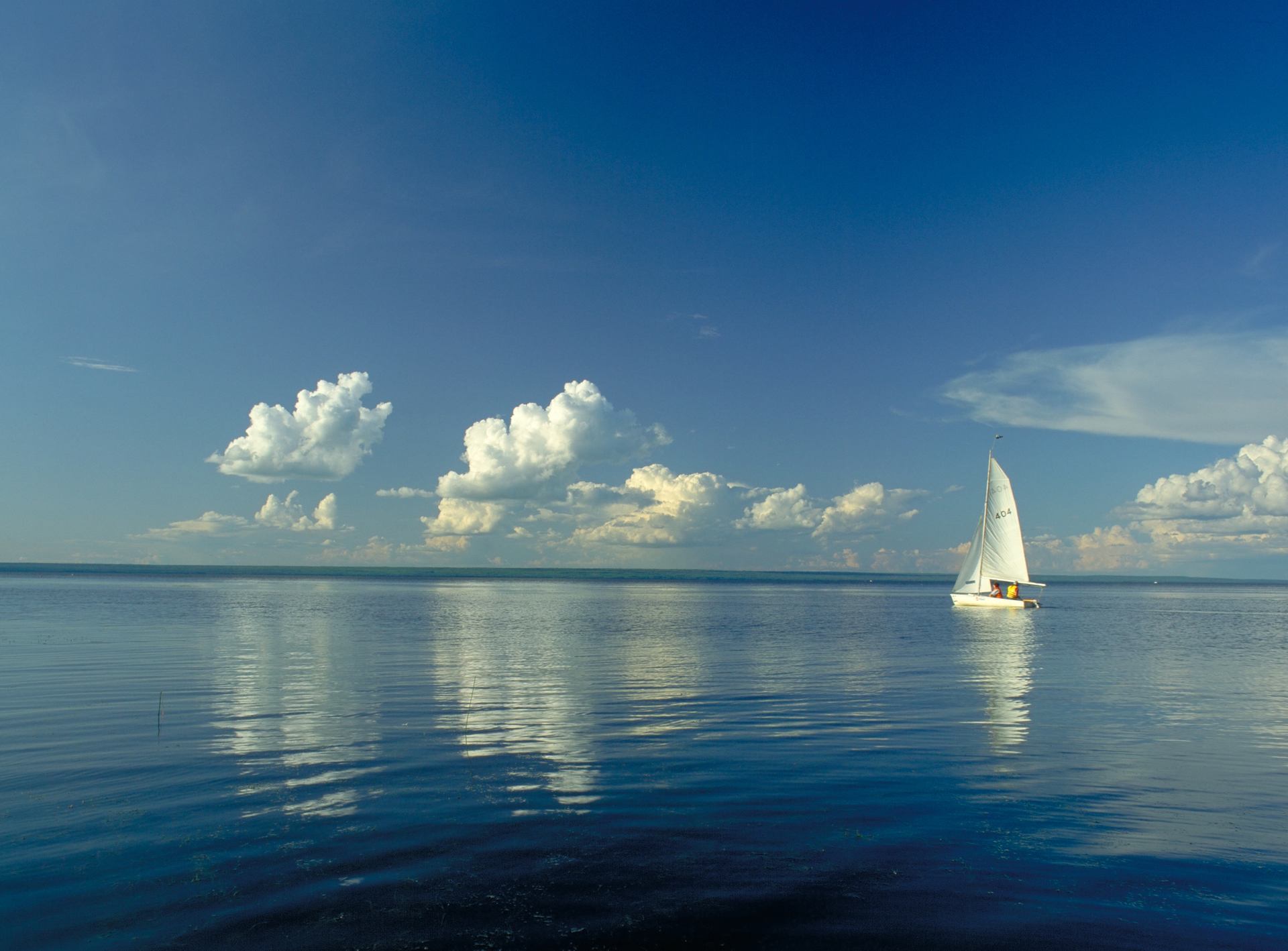 A sailboat on a calm lake with blue sky and clouds above.