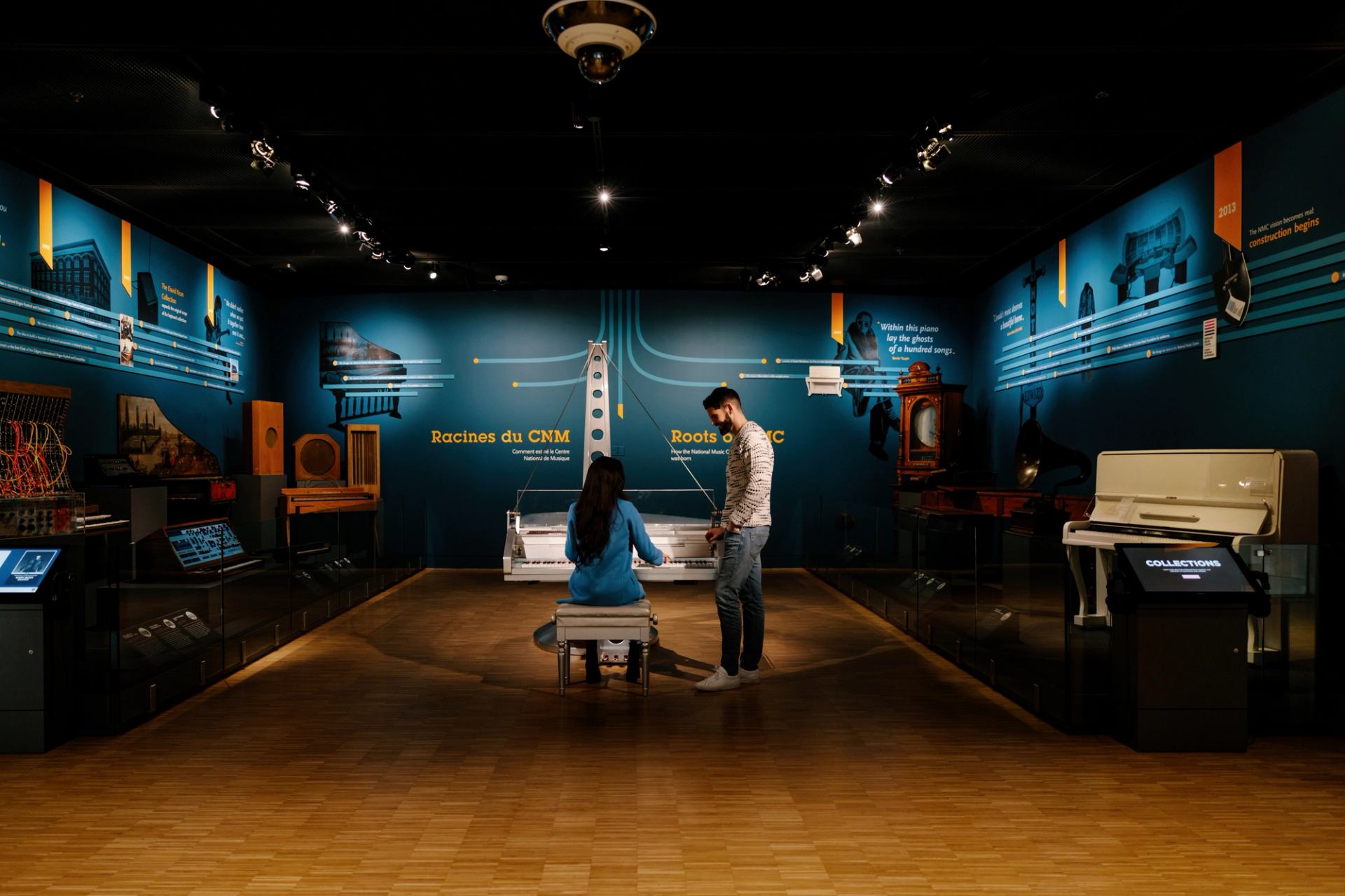 Visitors playing the piano at Studio Bell in a dimly lit exhibition room.