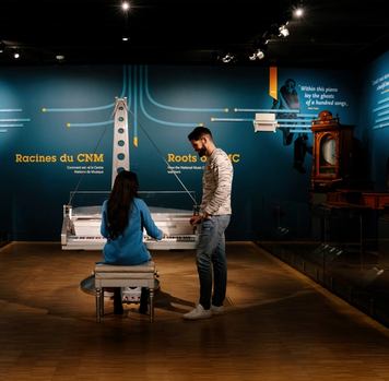 Visitors playing the piano at Studio Bell in a dimly lit exhibition room.