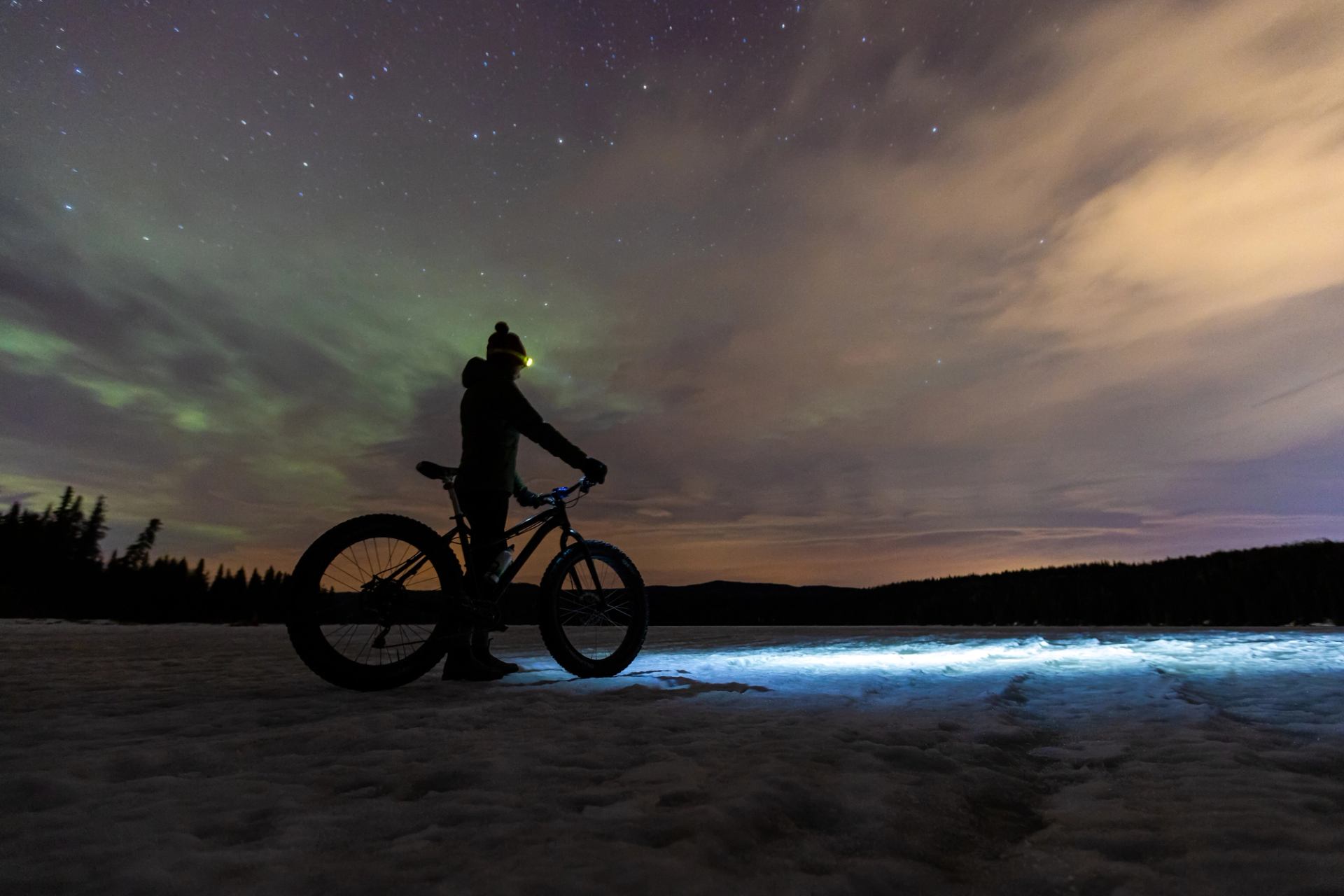 Person fatbiking at night and enjoying the Northern Lights and night sky near Hinton
