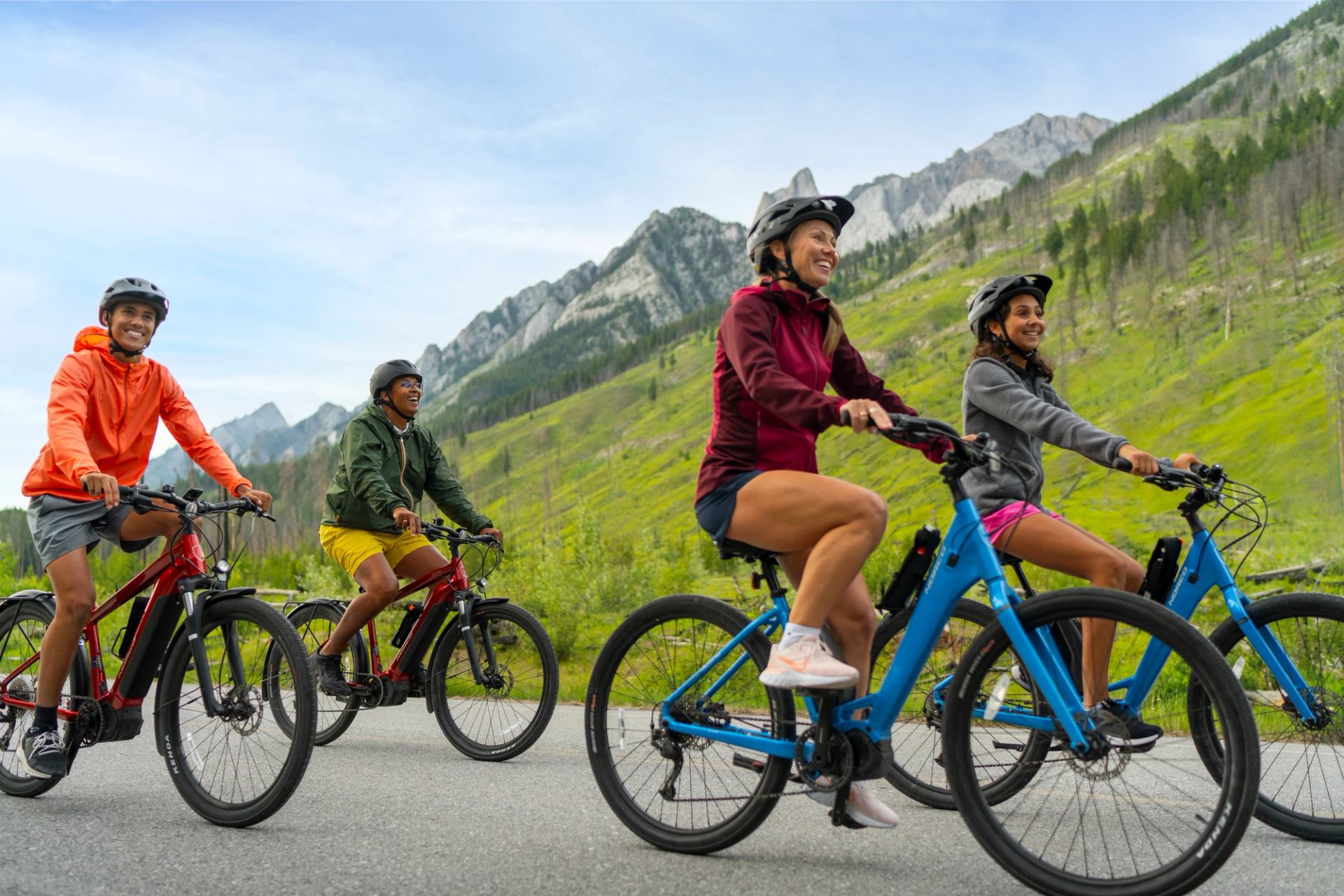 A family of four rides e-bikes on the car-free Bow Valley Parkway with mountains alongside the road.