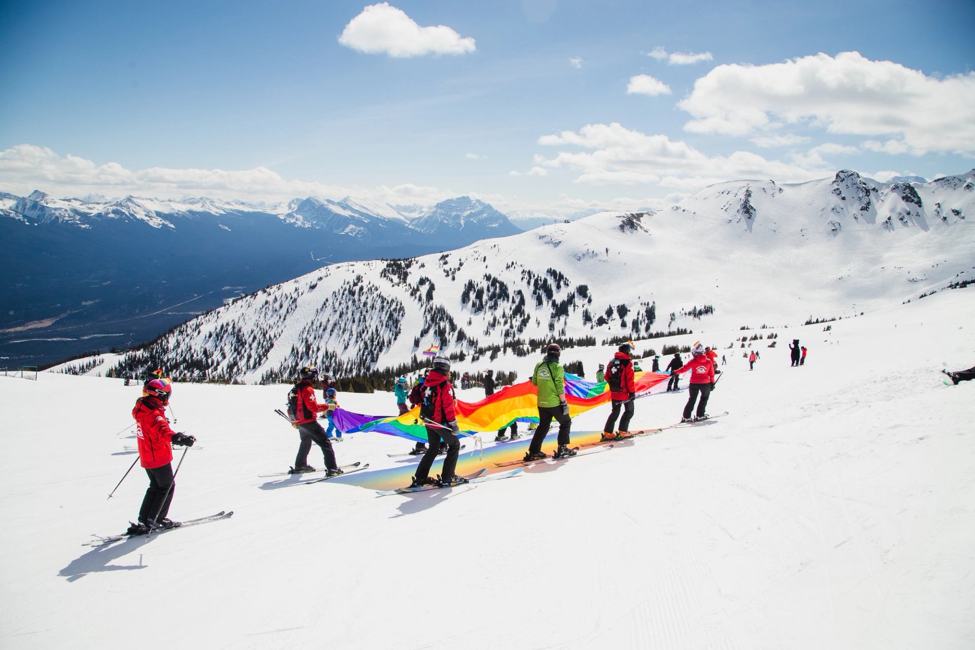 A group of skiers holding a pride flag as they ski in the mountains in Jasper.