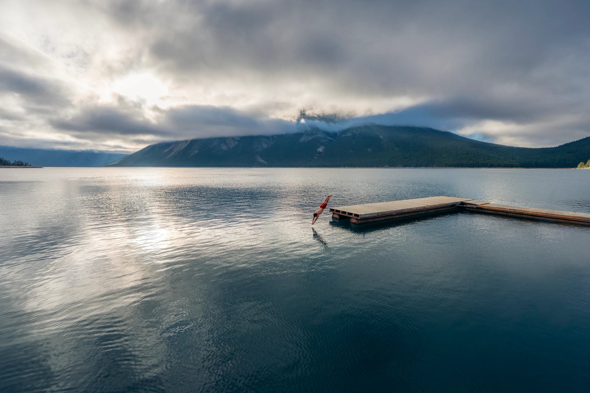 A man dives into Lake Minnewanka from a dock.