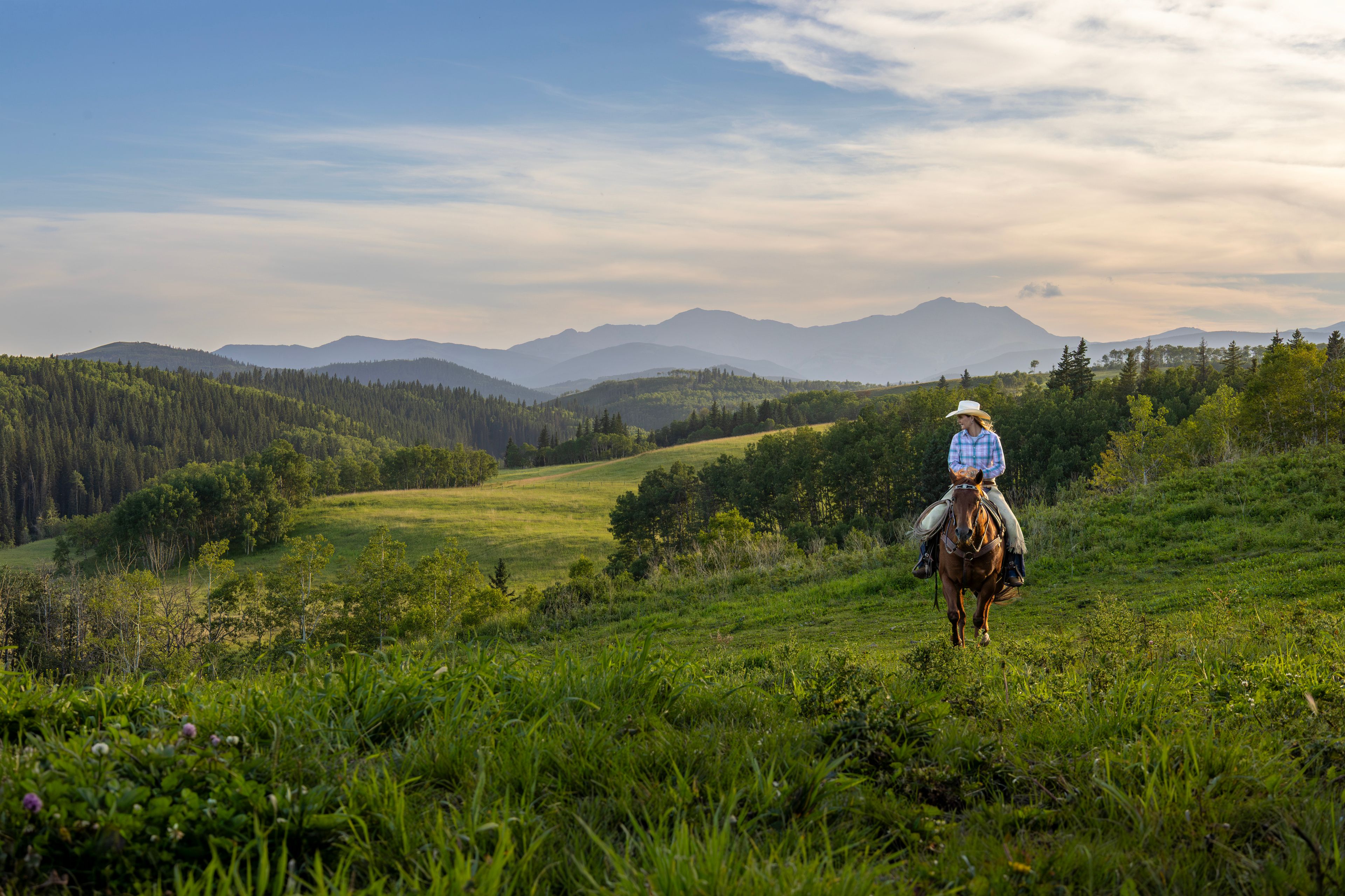 A woman rides a horse across a ranch at dusk
