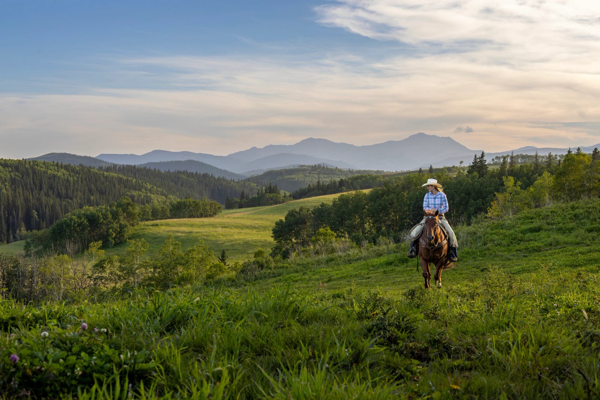A woman rides a horse across a ranch at dusk