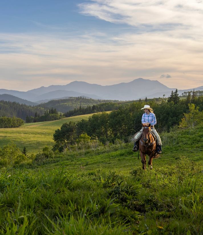 A woman rides a horse across a ranch at dusk