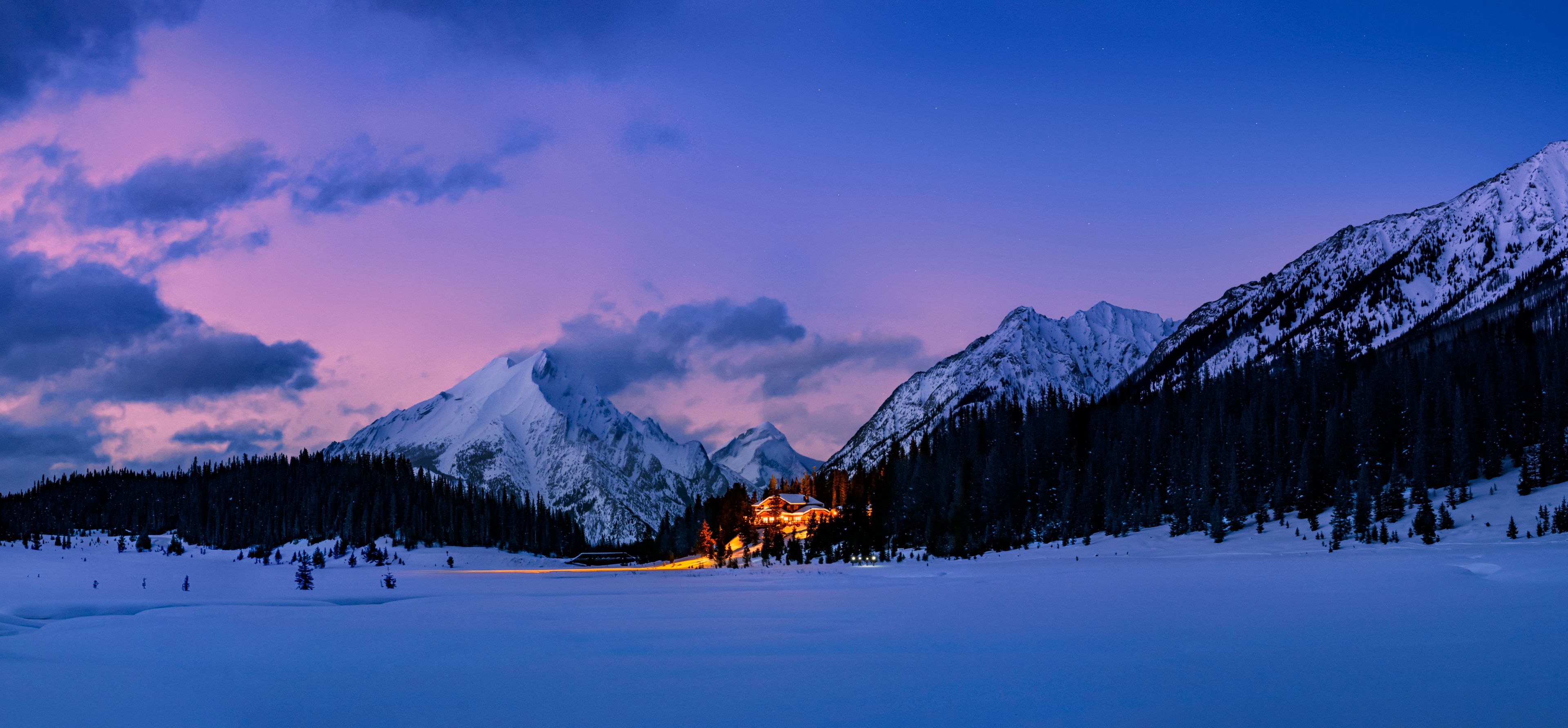 A large lodge lit up at dusk under a pink-blue sky.